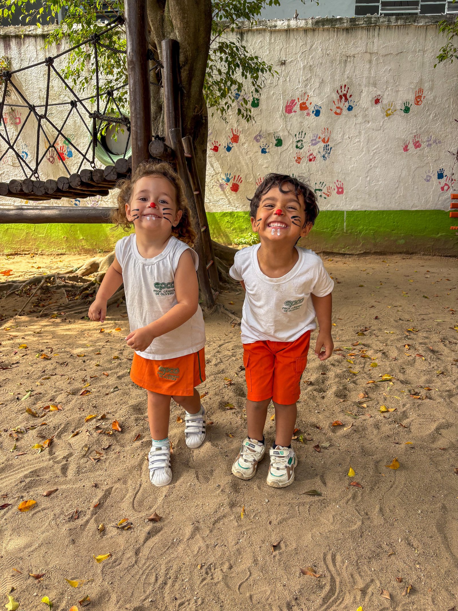 Dois amigos sorrindo com o rosto pintado no parque arborizado