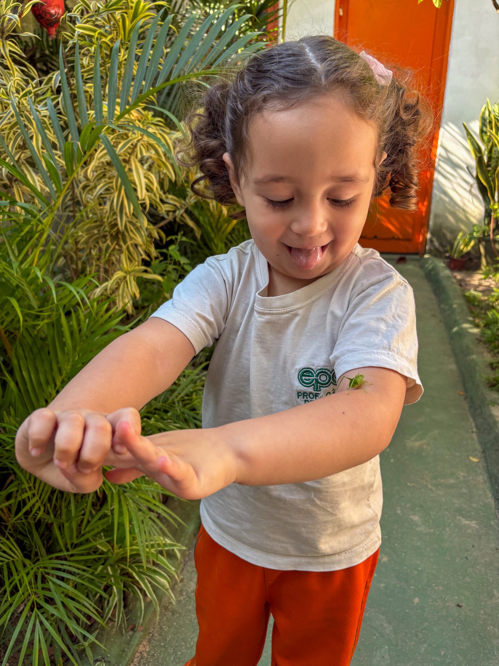 Aluna observando um inseto em seu braço entre as plantas
